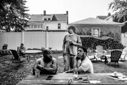 A black and white photo from a graduate student that is winner of the fellowship. Two men are sitting outside on a picnic bench while one man stands behind.