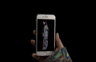 A hand holding an iPhone with an image of a person wearing holographic clothing