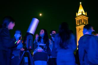 Students gather around the Unistellar eVscope 2 - a state-of-the-art telescope - at night for a star party. 