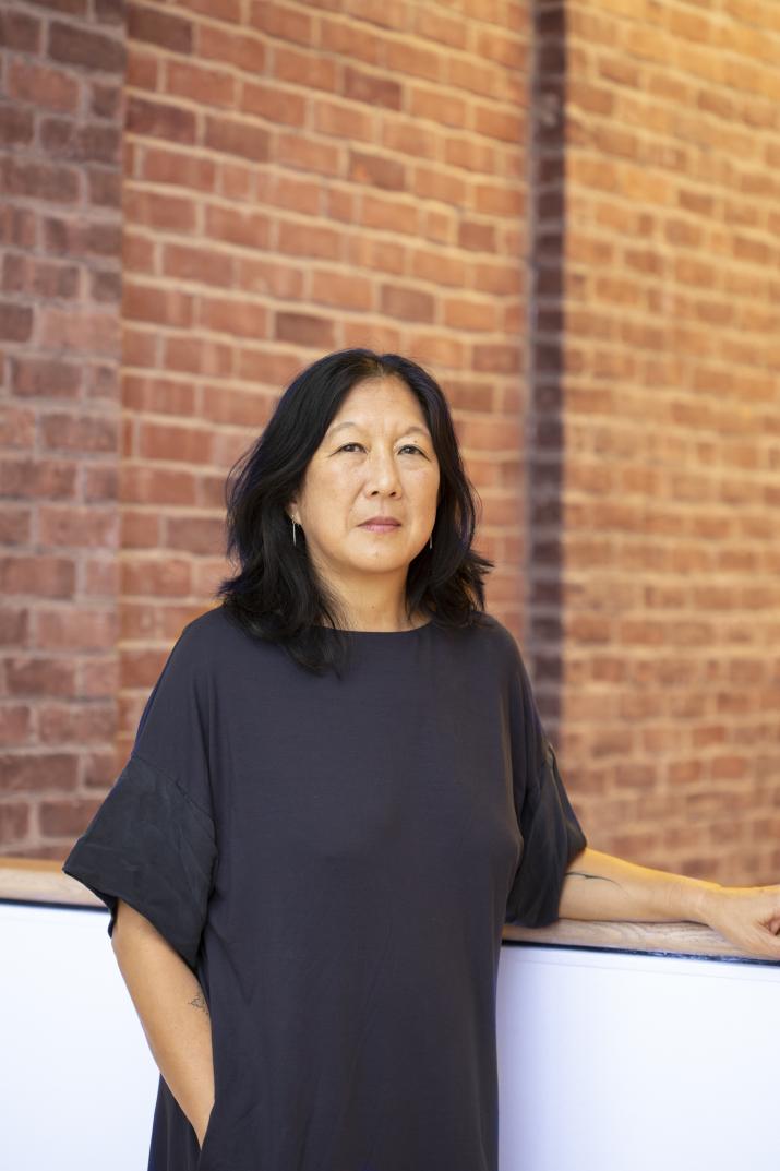 Christina Yang, wearing a black top, poses for a portrait in front of a brick wall.