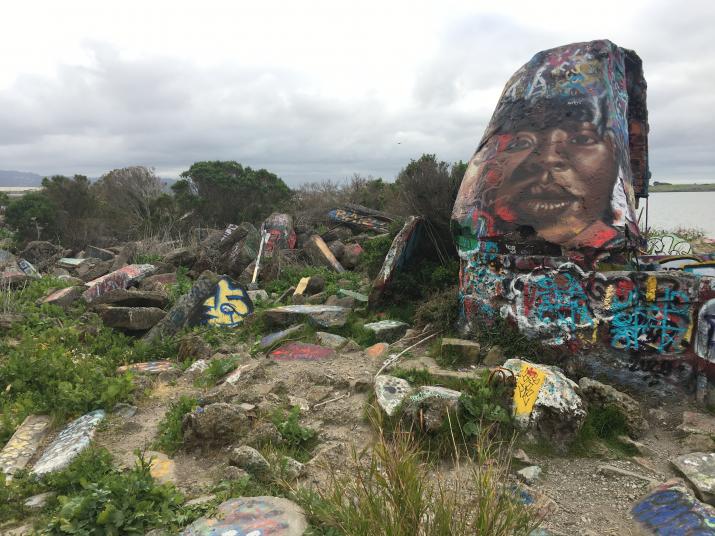 A painting of a woman is on a large rock, next to rubble on the ground