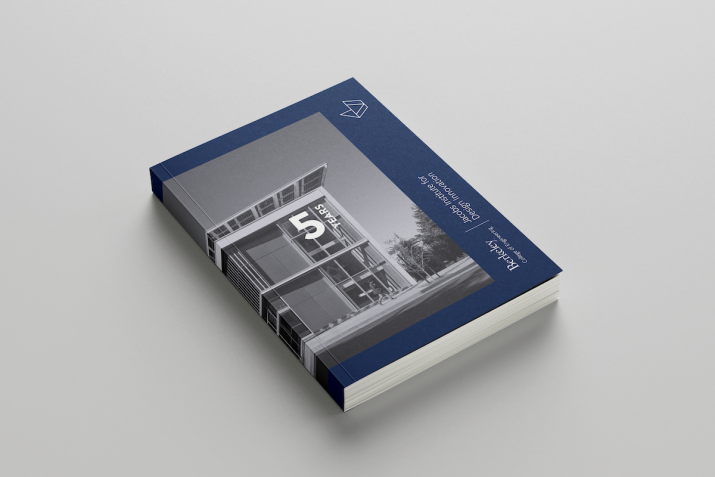 A book with a navy cover, image of the Jacobs institute's building, and the words, "5 years, Jacobs Institute for Design Innovation". The book lies on a gray surface.