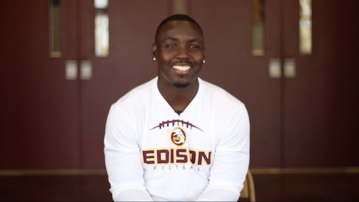 A football player smiling at the camera in a locker room.