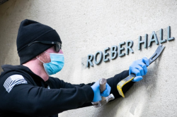 A worker at UC Berkeley removing the name "Kroeber Hall" from the exterior of the campus building.