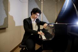 Joshua Kyan Aalampour sits in front of a piano, fingers touching the keys.