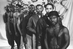 a black and white photo of filmmaker Marlon Riggs standing at the front of a line of Black men.